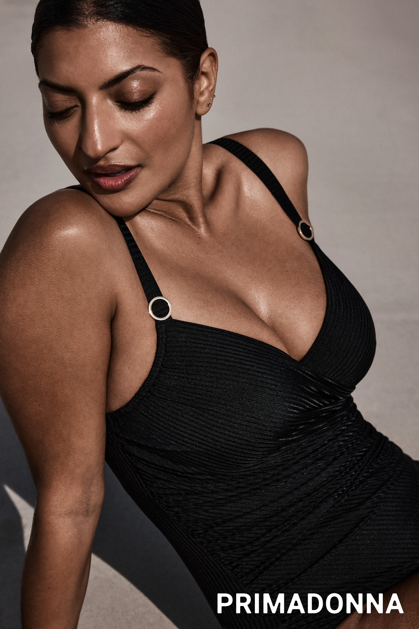 Eine Frau mit entspanntem Ausdruck trägt einen schwarzen Badeanzug mit goldenen Details