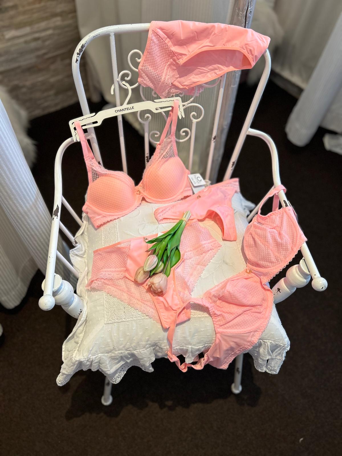Zarte rosa Dessous liegen dekorativ auf einem weißen Stuhl mit drei Tulpen