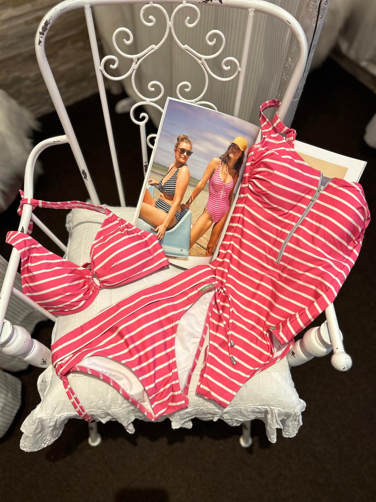 Zwei pinkweiß gestreifte Bikinis liegen auf einem weißen Stuhl neben einem Foto von zwei Frauen im passenden Badeoutfit
