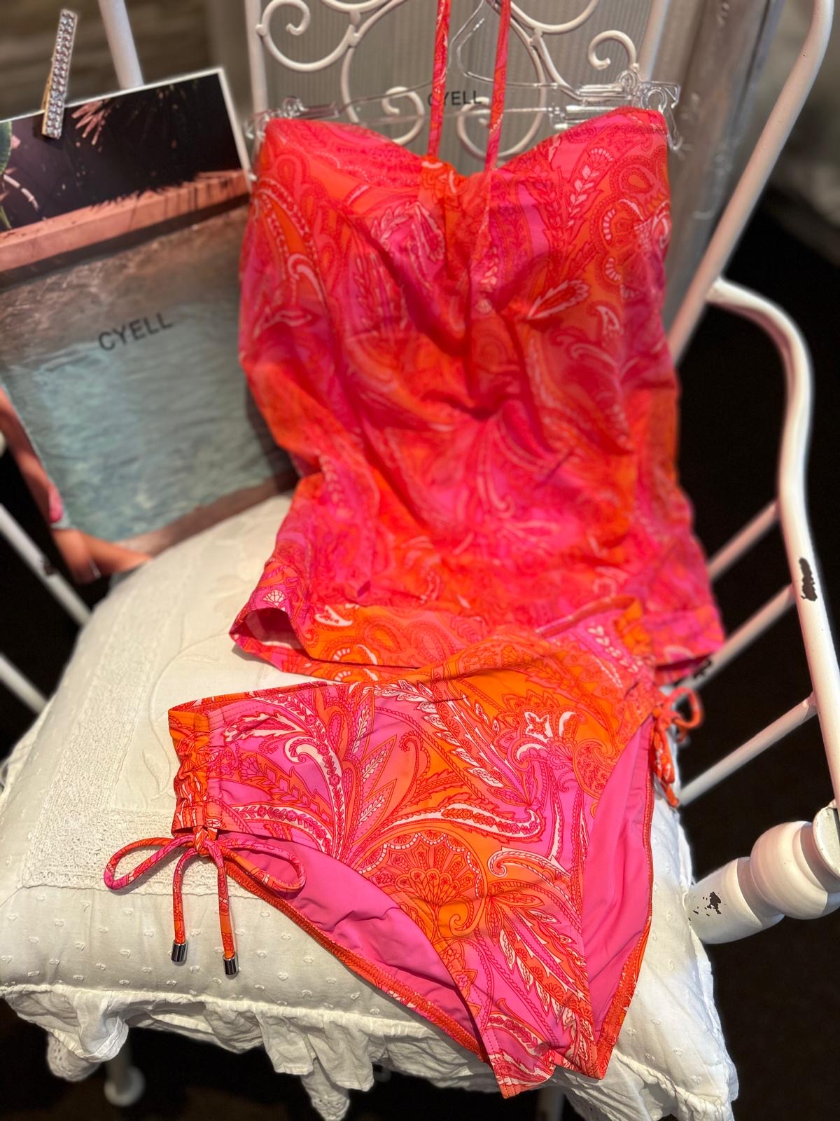 Ein sommerliches, pink-orange gemustertes Bikini-Set liegt dekorativ auf einem hellen Stuhl